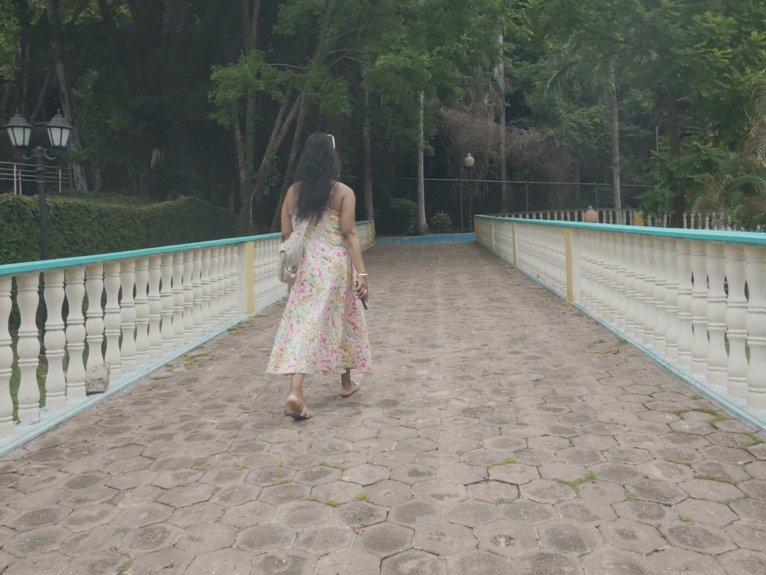 Electa walking down a garden bridge while traveling and exploring a lush destination.