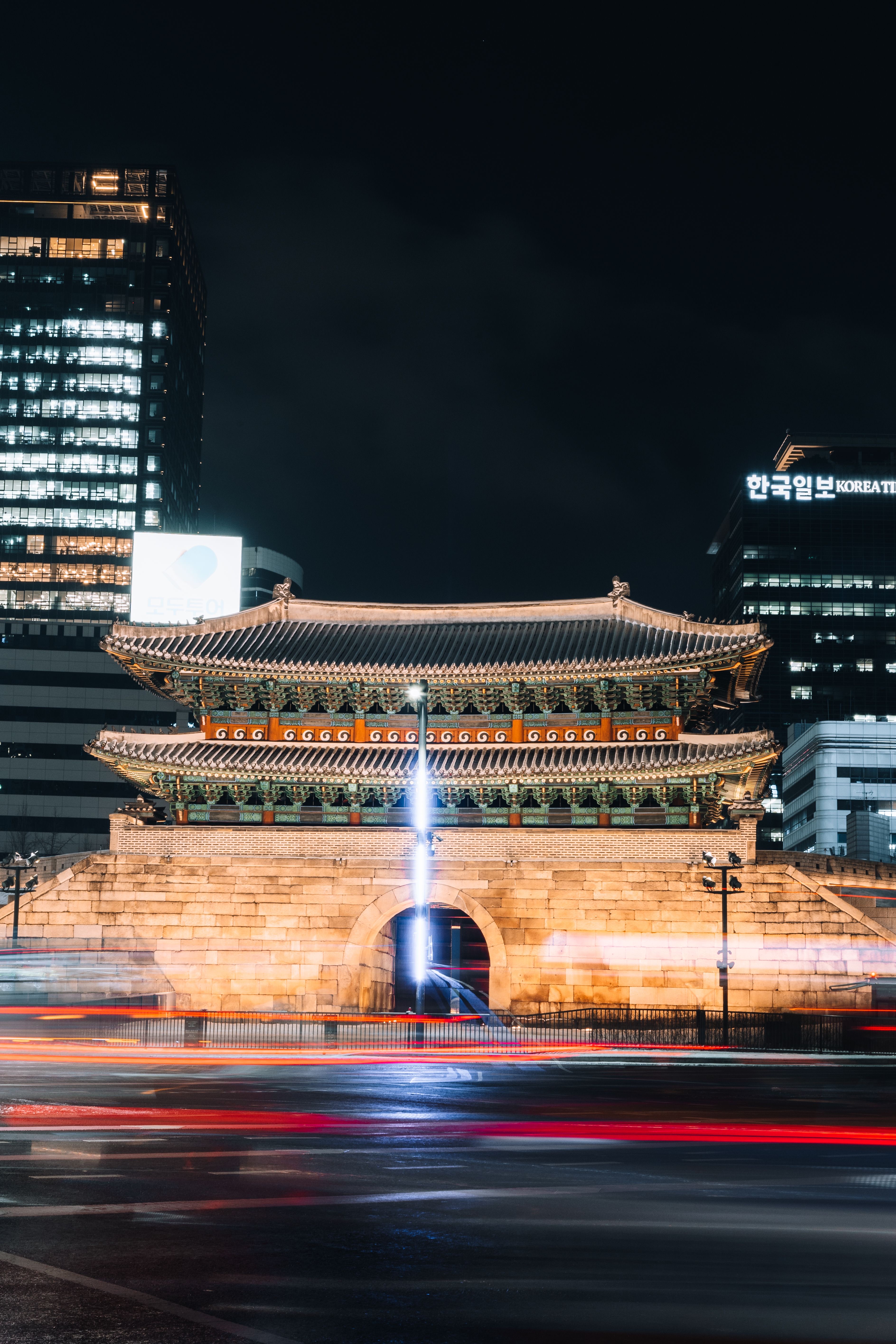 Traditional Korean architecture lit up at night beside modern city towers in Seoul.